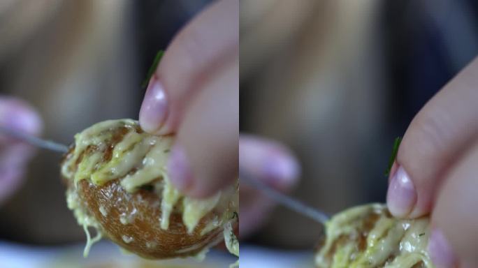 女性的手用叉子把蜗牛从海螺壳里拽出来。宏。垂直视频。这个女孩吃蜗牛配奶酪