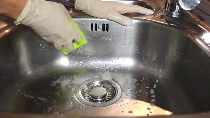 一个戴着手套的女人用海绵擦拭厨房里的金属水槽。