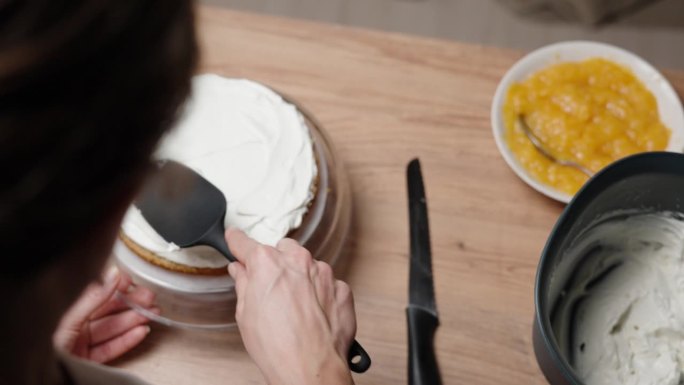从头部后面，慢镜头显示了这位女士正在准备蛋糕，在海绵蛋糕上涂上奶油。