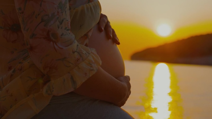 孕妇的腹部摸她的腹部隆起的海洋和天空。美丽的日落