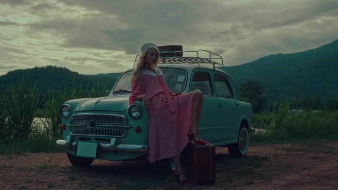 一个穿着粉色复古连衣裙的女孩坐在一辆绿松石色复古车的引擎盖上