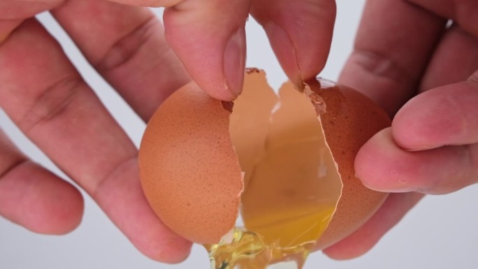 男人用手捏鸡蛋做煎蛋卷。一个人在做鸡蛋当早餐。雄手敲鲜蛋黄近距离。