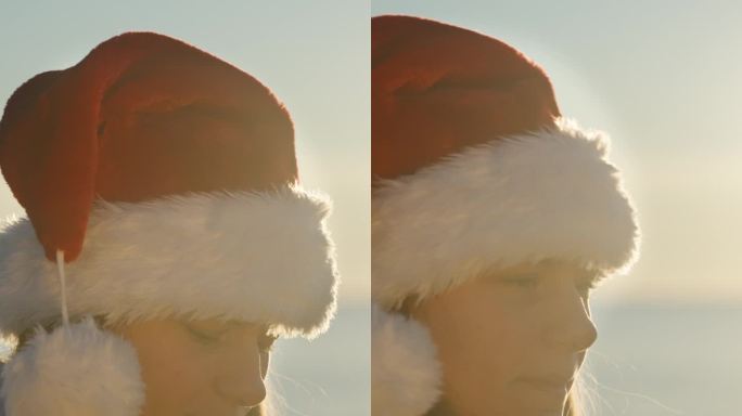 垂直视频。圣诞节的早晨，一位戴着圣诞老人帽的年轻女子在海边享用姜饼饼干和茶。明亮的阳光在她身后。