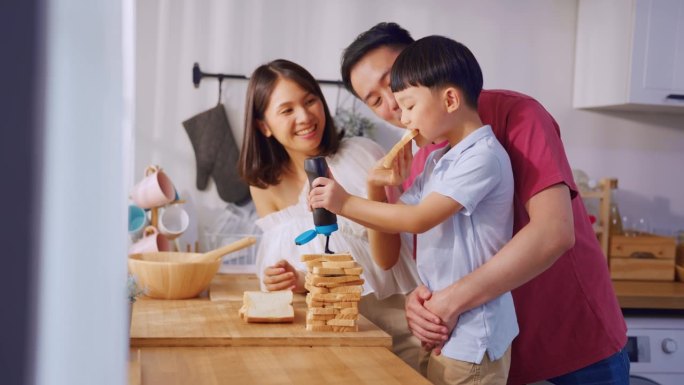 漂亮的亚洲夫妇带着年幼的儿子在家里的厨房里烤面包。幸福的家庭，爸爸和妈妈花时间和小儿子一起做巧克力面