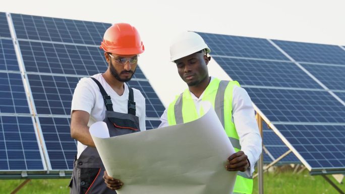 年轻的非洲工程师和印度技术人员站在那里，计划安装太阳能电池板。产业工人讨论安装太阳能系统