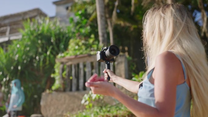 女旅游博主在海边拍摄视频。金发女郎在热带岛屿上用专业相机拍摄博客。影响者为社交网络记录故事。Vlog