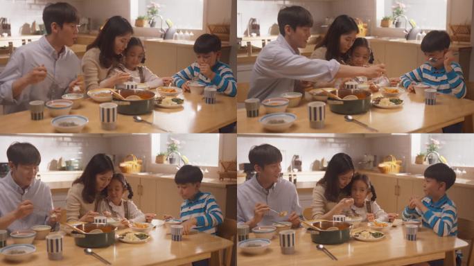幸福的韩国四口之家在家里的厨房里一起享受美味的饭菜。父母和他们可爱的孩子聚在一起吃午饭，边吃边聊