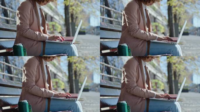 女商人在手提电脑上工作，在街边长椅上做笔记