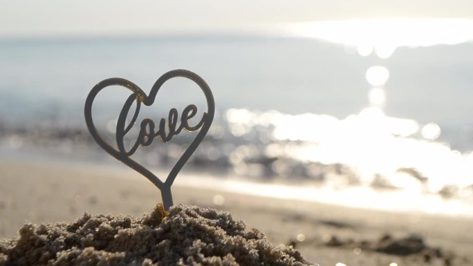 爱心和文字形状的塑料棒在沙滩上的沙滩上，在阳光明媚的夏日的海边，特写镜头。以海浪为背景的爱心字人物。
