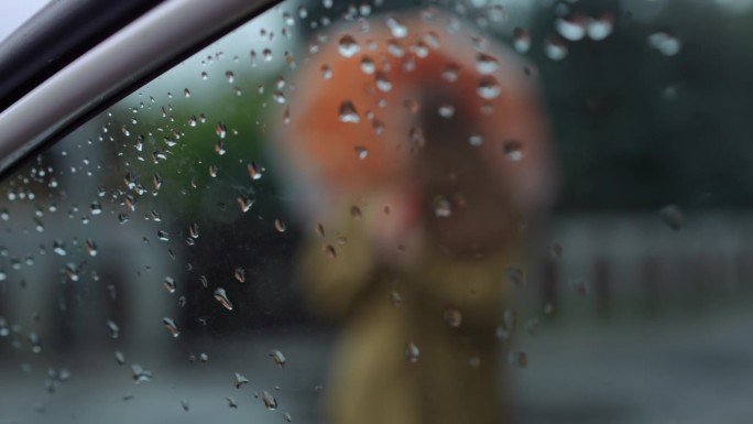 雨打在车窗玻璃上，背景是模糊的女子举伞的慢动作。不明身份的白人年轻女子在下雨天戴着配饰。
