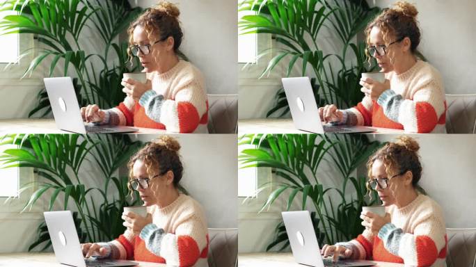一位女士一边用笔记本电脑工作，一边在喝饮料前吹着热茶。宁静工作者在线开始工作的人喝咖啡或茶。家庭办公