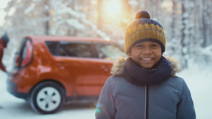 冬天，穿着暖和衣服和帽子的男孩站在红色的汽车背景中
