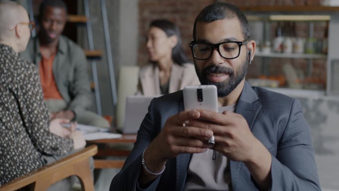 快乐的企业家坐在现代咖啡馆里用智能手机发短信