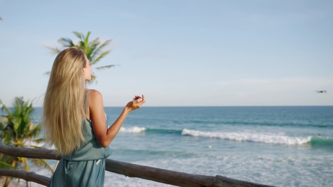 无人机拍摄金发女子视频博主在热带岛屿上与海景交谈。斯里兰卡的女视频博主在无人机上拍摄视频。旅行者在慢