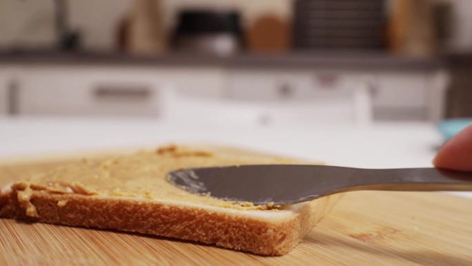 小刀把花生酱涂在烤面包上，这是一种经典的美式三明治制作方法