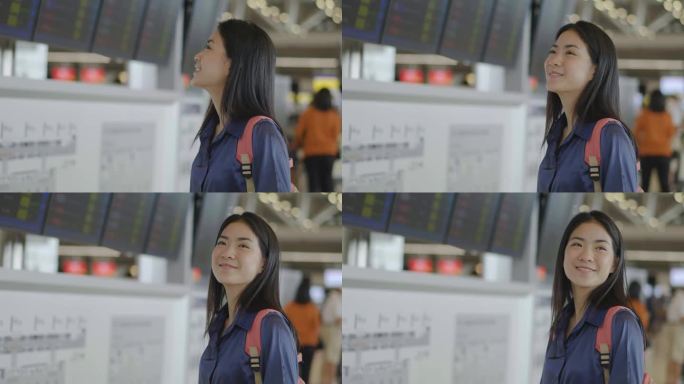 手持护照和登机牌的年轻亚洲女性站在机场候机楼的航班时刻表前，看着航班信息板，检查航班