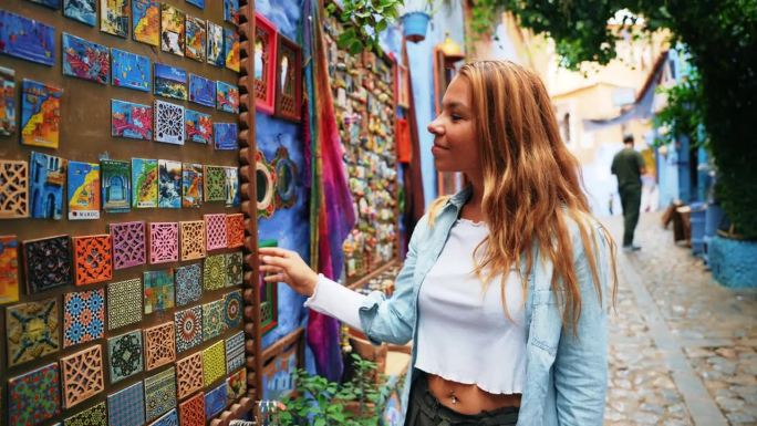 一名年轻女子在户外市场看着一面漂亮的小镜子和一件五颜六色的布料