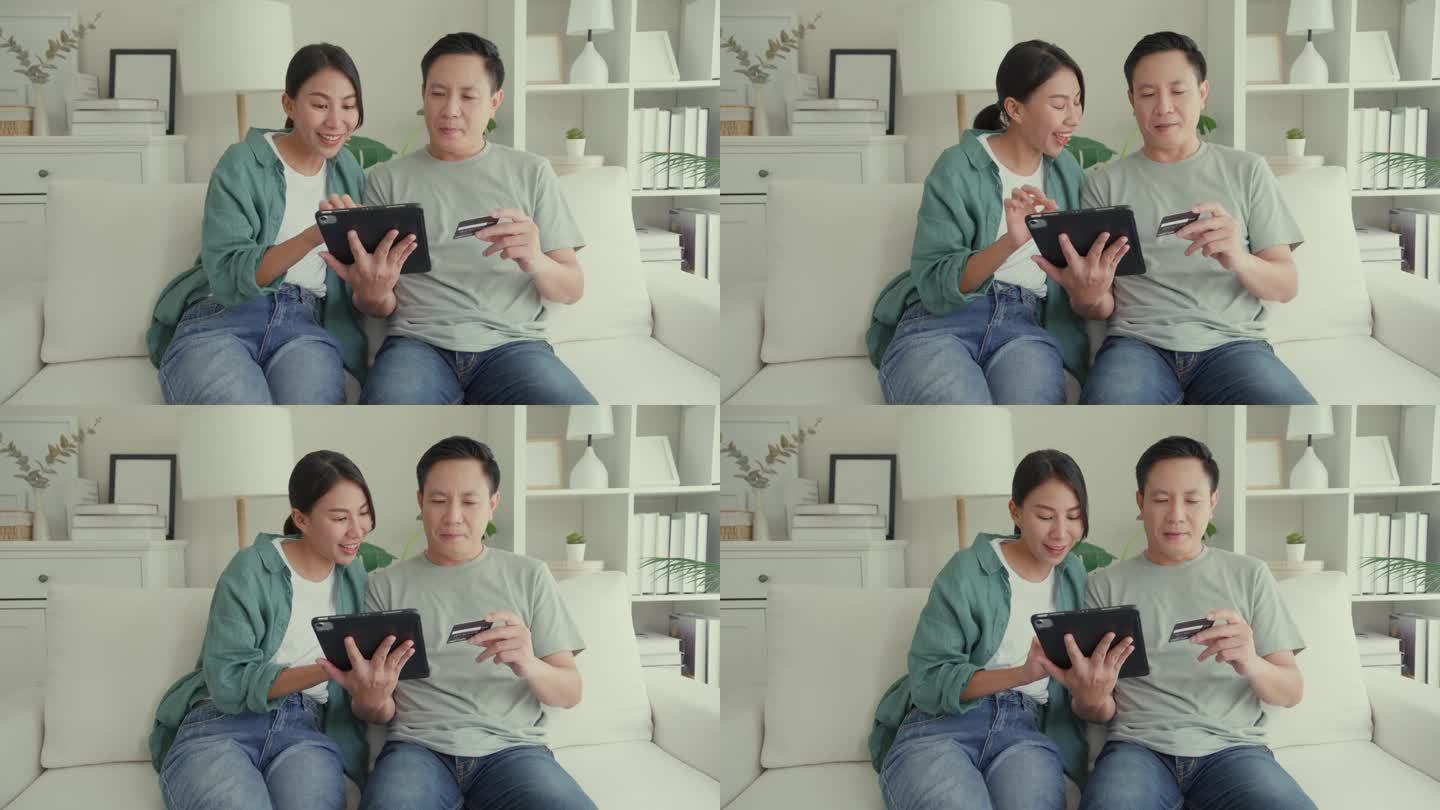 幸福的亚洲夫妇一起坐在家里客厅的沙发上玩电子平板设备购物，使用信用卡在线支付。生活方式花时间在家里。