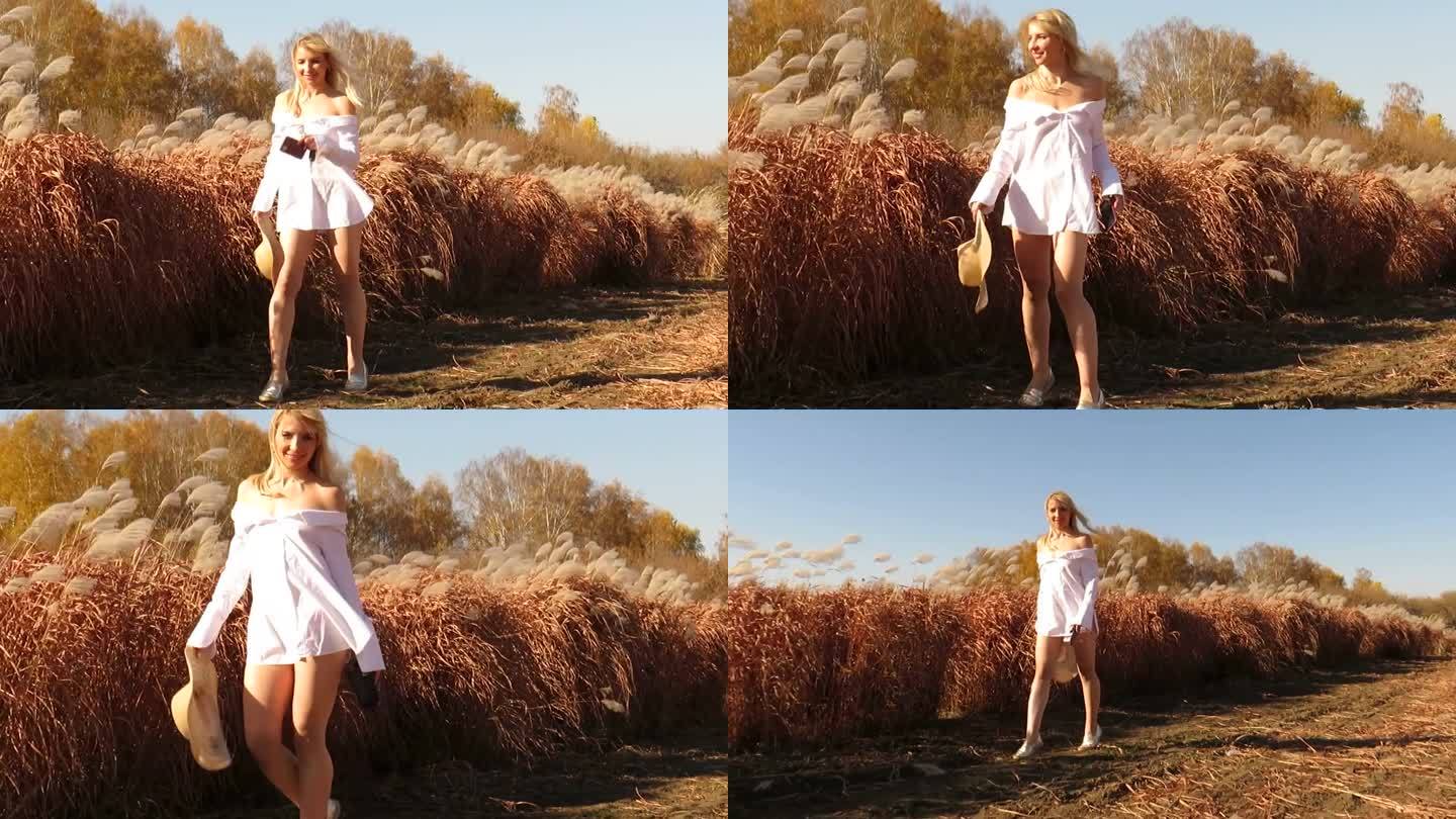 一位穿着白色短衬衫的迷人的年轻女子在秋天的城外田野里散步