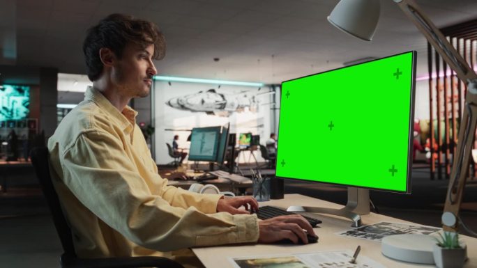 创意高加索人的肖像坐在桌子上使用桌面电脑与模拟绿屏铬。在游戏设计初创公司工作的男性概念美工，创造沉浸