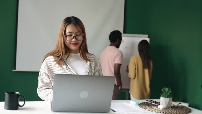 年轻的微笑的女人在现代化的办公室工作，使用笔记本电脑