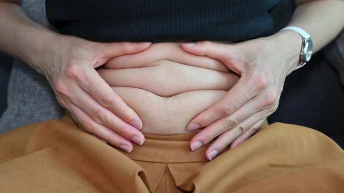 女人在吃完东西后抚摸和玩耍她的大肚子的特写。