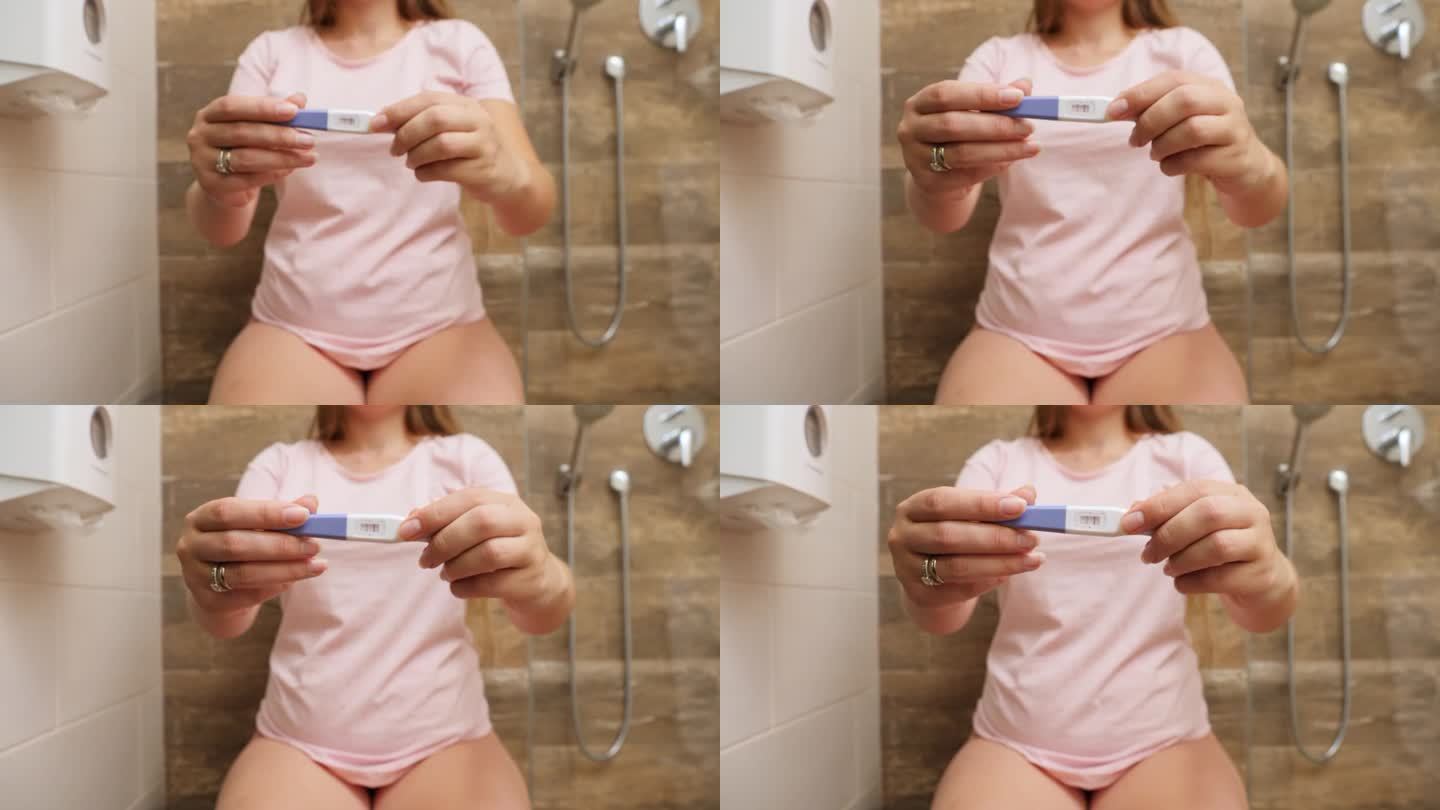 一名年轻的孕妇坐在马桶上，镜头中的两道条纹显示怀孕测试呈阳性