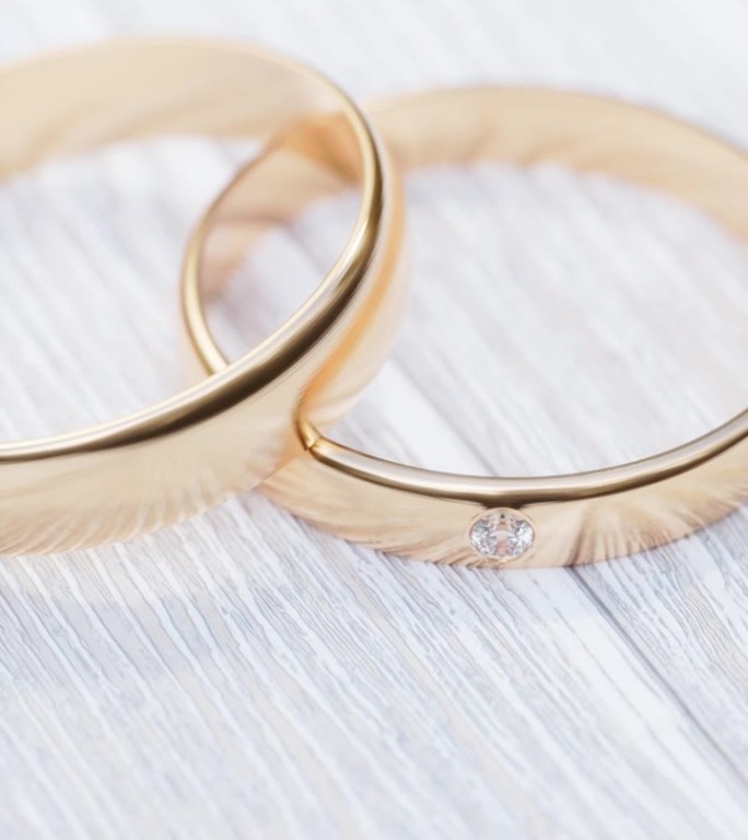 把相机绕着两个金结婚戒指旋转。两个金色的结婚戒指放在一张白色的木桌上。3 d渲染。