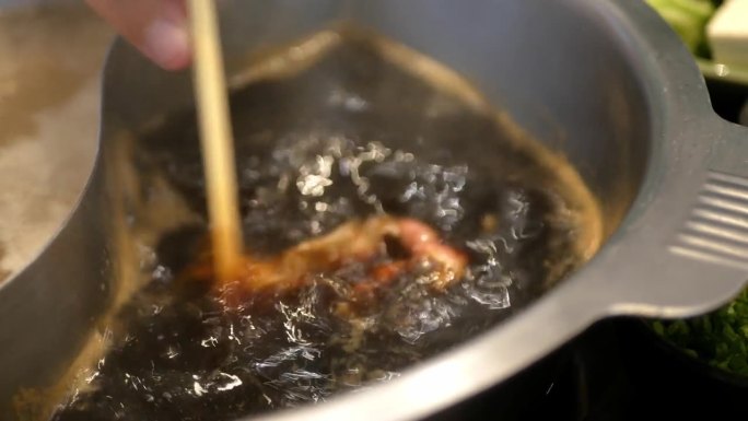 用筷子夹肉、牛肉片在滚烫的火锅汤中烹煮的蔬菜火锅特写。日本亚洲美味健康火锅涮食品