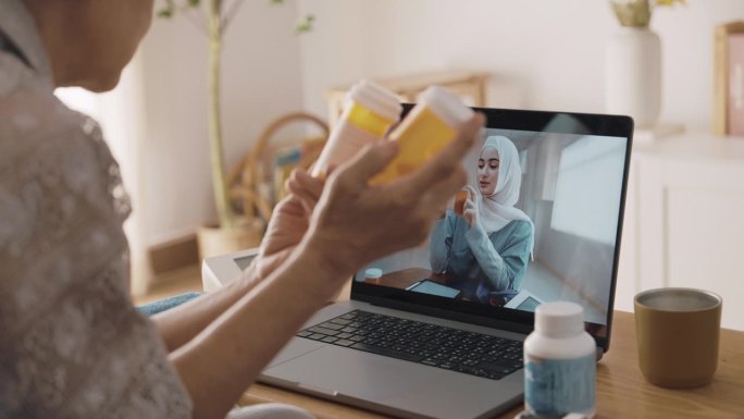 老年妇女在家用视频聊天的同时，集中精力倾听女医生对自己药物的提问。