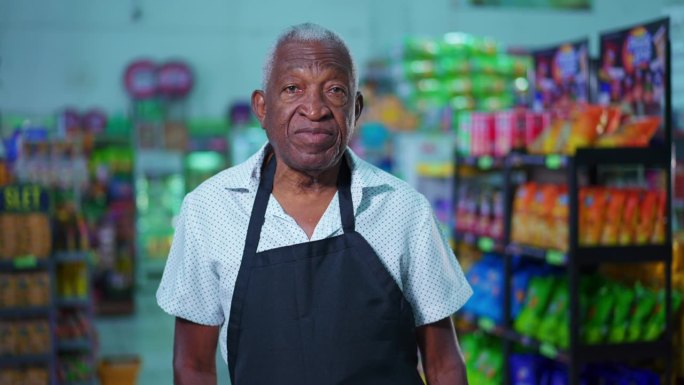 一名超市资深黑人男性员工站在超市内，系着围裙，表情中性。杂货店工作人员的非裔美国人肖像