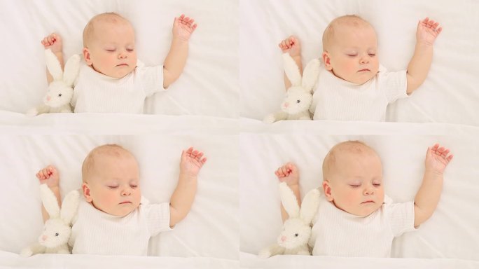 可爱的小新生宝宝抱着毛绒兔子睡在毯子下，甜蜜健康的宝宝睡在白色的婴儿床上，一个文字的地方