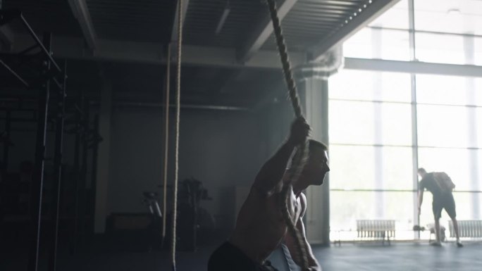 强壮的男人在健身房爬绳子，训练他的身体，赤裸的躯干与救济肌肉