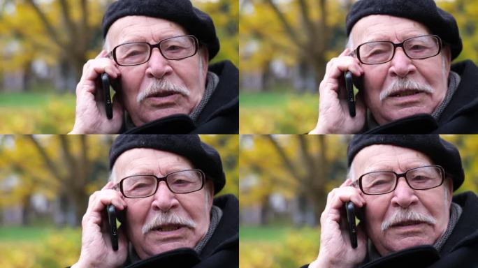 一位和蔼可亲的白发老人戴着眼镜，坐在公园的长椅上讲电话