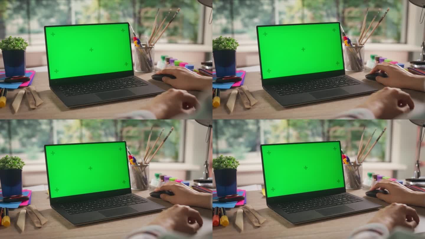 在肩膀上的镜头与Illustrator使用笔记本电脑模拟绿屏Chromakey显示。艺术学生坐在桌子