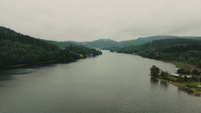 无人机飞过宽阔的河流，展现了忧郁天气下美丽宁静的北欧绿色森林和峡湾