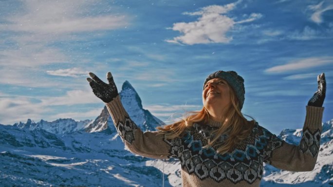 一个女人在山坡上向空中抛雪，背景是马特洪峰