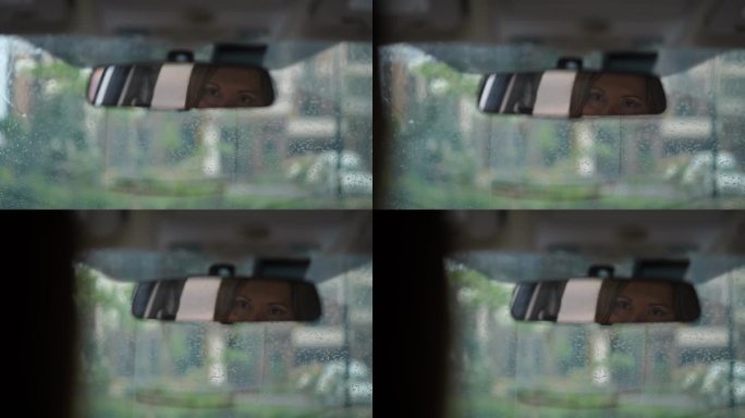 车内的后视镜特写，深色皮肤的女人棕色的眼睛望向别处。下雨天坐在车里的白人女士在外面思考。