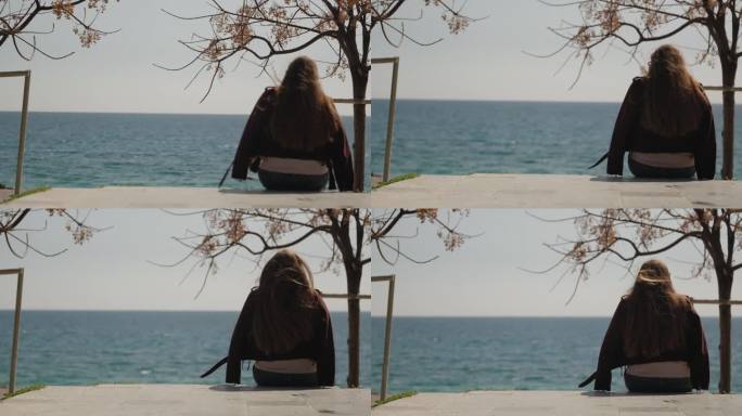 一位年轻女子坐在海边的混凝土上，望着远方。风吹乱了她的长发。