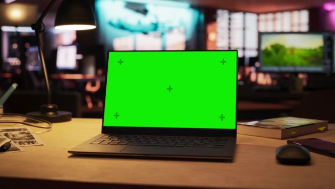 放大镜头的笔记本电脑站在木桌子与绿色屏幕Chromakey模拟显示器。创意办公室及工作环境激发创意及