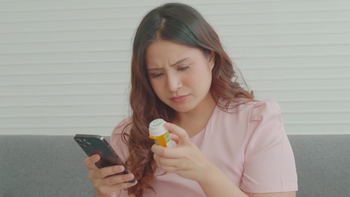 一名女子拿着药瓶在智能手机上查找药物信息。