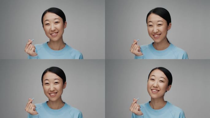 年轻的韩国妇女在彩色摄影棚里看着相机的肖像。成年日本女孩孤独的灰色背景特写。亚洲人微笑，用手指表示爱