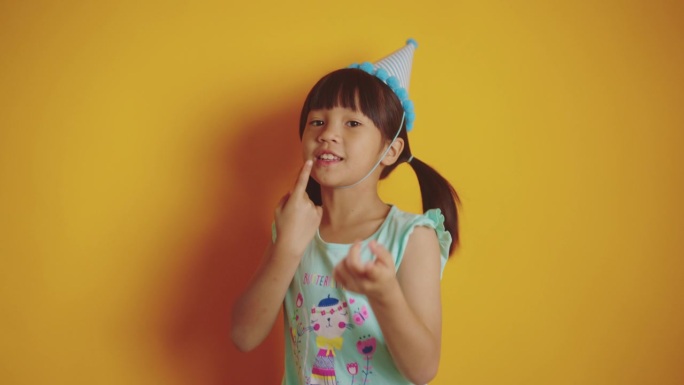 可爱的女孩戴着黄色背景的生日帽。