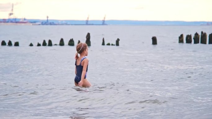 无人看管的白种小女孩穿着泳装走进海水玩破浪