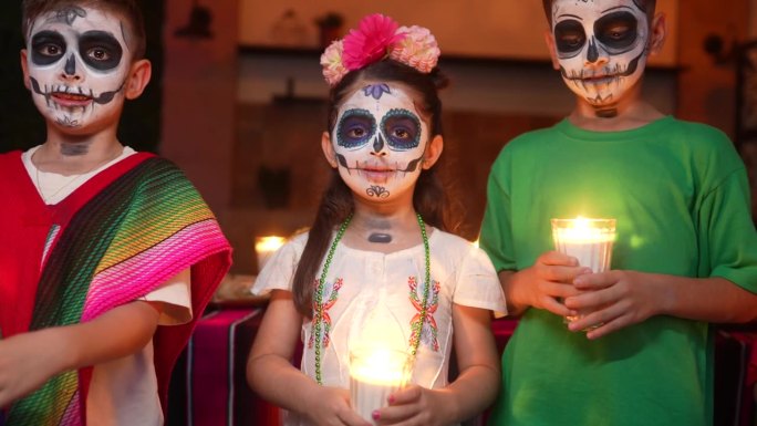 孩子们的肖像，脸上画着糖头骨，在死者的庆祝活动中拿着蜡烛