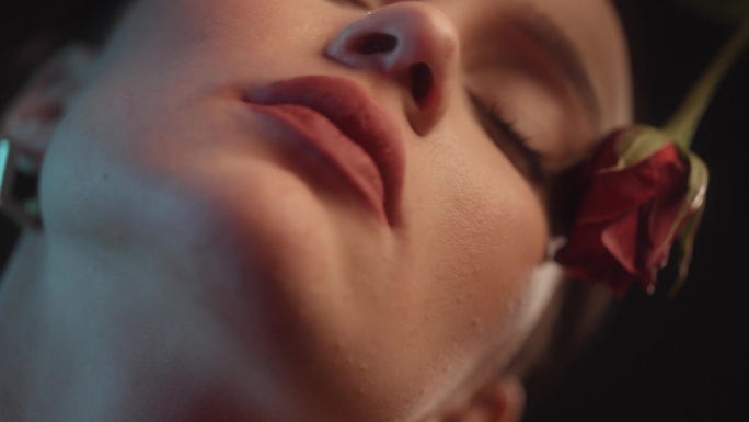 性感的女人用红色的口红和纹身黑色背景工作室拍摄跳舞与一个单一的红玫瑰花和压花瓣对皮肤