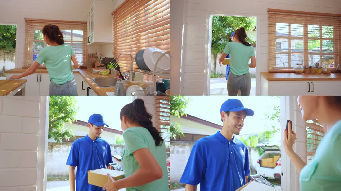 亚洲年轻的快递员在家里给女顾客送包裹。穿着蓝色制服的迷人邮递员正在工作，把一盒水果和蔬菜杂货送到家门