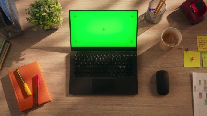 从上往下看一台笔记本电脑，配有模拟绿屏Chromakey显示屏和运动追踪器，它站在一张木制办公桌上，