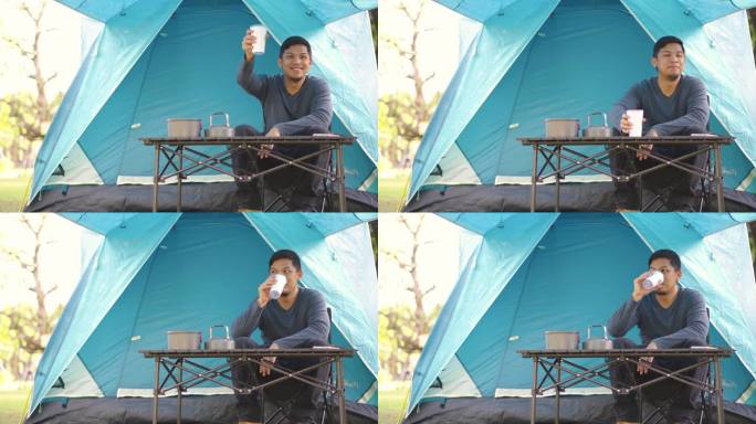 一名亚洲男子坐在露营帐篷前，一边喝着热咖啡，一边在森林露营地休息和放松。
