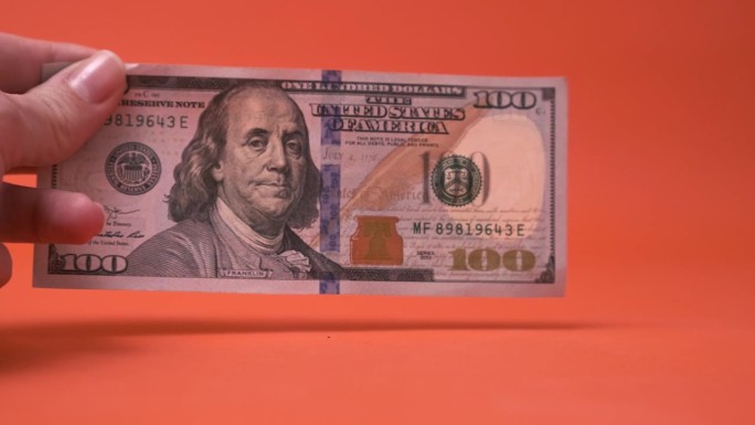 一个女人的手拿着一张红色背景的百元大钞。我们的货币。股市，世界经济。贷款。储蓄，货币坚挺可靠。本杰明